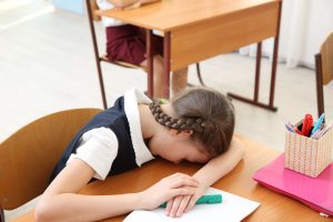 Portrait,of,tired,elementary,schoolgirl,sleeping,on,desk,in,classroom