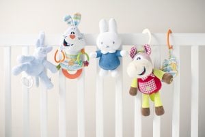 Five,soft,colorful,toys,at,white,children's,bed.