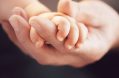 closeup,of,a,baby,holding,man's,finger,against,black,background