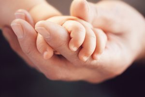 closeup,of,a,baby,holding,man's,finger,against,black,background