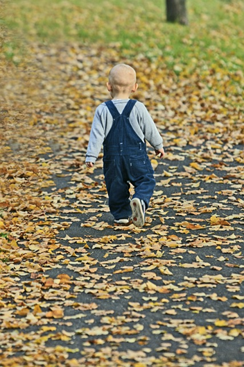 Дете се разхожда на пътека с паднали есенни листа